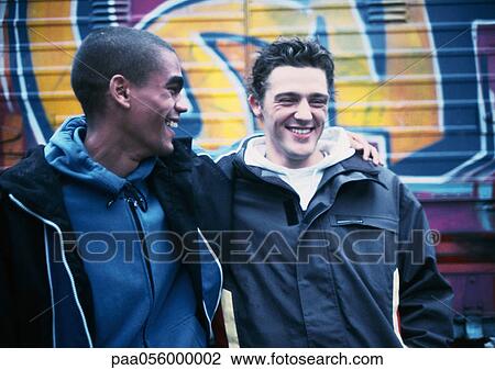 Stock Image - Two young men, one with arm around the other, smiling. Fotosearch