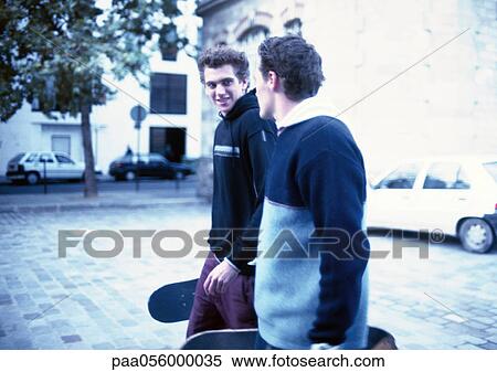 Stock Photography - Two young men walking in street, holding skateboards. Fotosearch