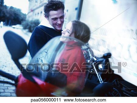 Stock Image - Young couple embracing next to scooter in city street. Fotosearch