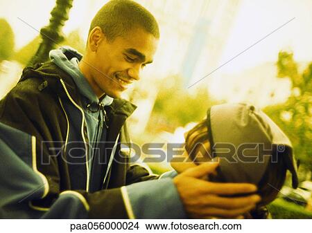 Picture - Young man holding young woman's head in hands, in street, side view. Fotosearch