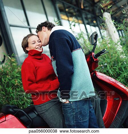 Stock Photo - Young man kissing young woman next to scooter. Fotosearch