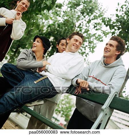 Stock Image - Young people grouped around bench in park, tilt. Fotosearch