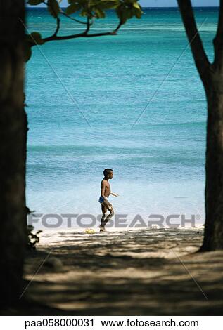 Stock Image - Boy walking on beach, sea in background. Fotosearch
