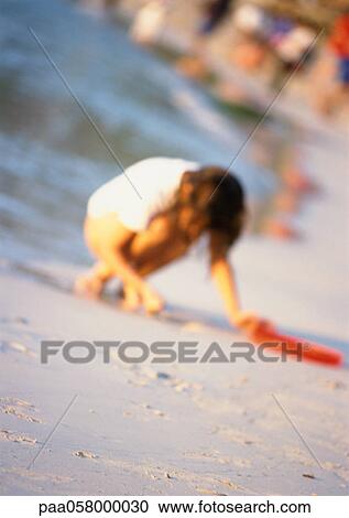 Stock Image - Girl crouching on beach, blurred. Fotosearch