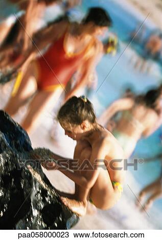Stock Image - Girl digging in sand, people and sea in background. Fotosearch