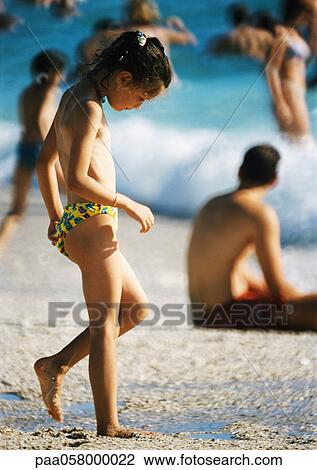 Stock Image - Girl on beach, looking down, people and sea in background. Fotosearch