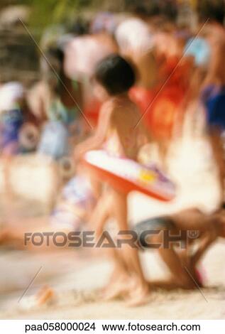 Picture - Girl wearing rubber ring on beach, people in background, blurred. Fotosearch