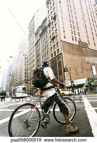Stock Photo - Man riding bike in street, buildings in background. Fotosearch