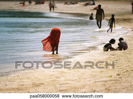 Stock Photo - People on beach, woman bending over, ankledeep in water. Fotosearch