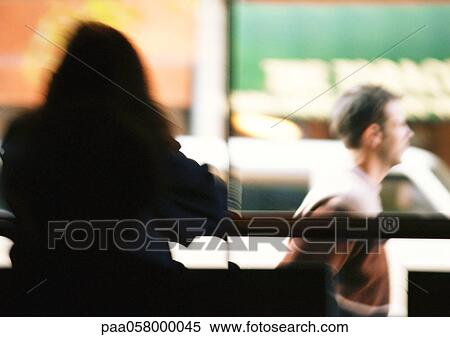 Stock Photography - Silhouette of woman sitting, man walking in background, blurred. Fotosearch