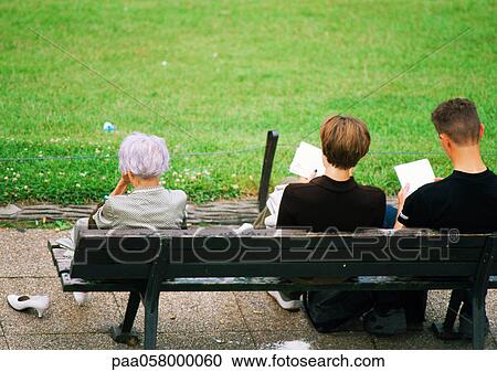 Stock Image - Three people sitting on bench, rear view. Fotosearch