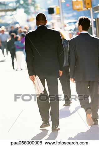 Stock Photo - Two businessmen walking in street, rear view. Fotosearch
