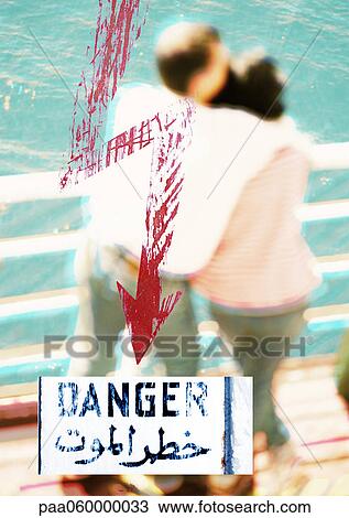Drawing - Couple standing by rail with red arrow, arabic text and "danger" text, montage, close-up. Fotosearch