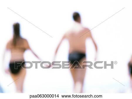 Man and woman holding hands at beach, rear view, blurred in distance. View Large Photo Image Picture - Man and woman holding hands at beach, rear view, blurred in distance.. Fotosearch