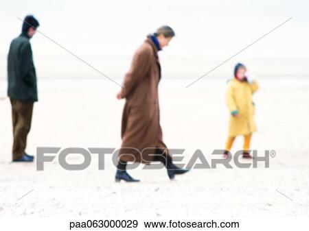 Stock Photo - People in coats walking on beach, blurred. Fotosearch