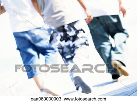 Stock Image - Three people walking, rear view, close up, blurred.. Fotosearch