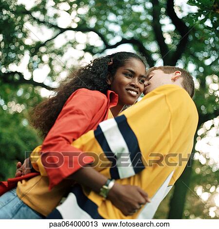 Young couple embracing outdoors, man whispering into young woman's ear, low angle view View Large Photo Image Stock Image - Young couple embracing outdoors, man whispering into young woman's ear, low angle view. Fotosearch