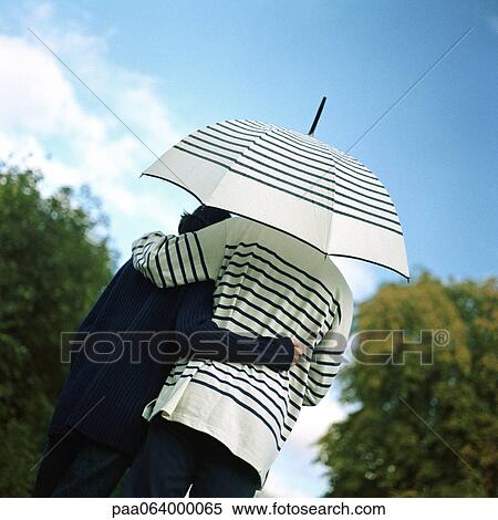 Stock Photography - Young couple underneath umbrella outside, rear view. Fotosearch