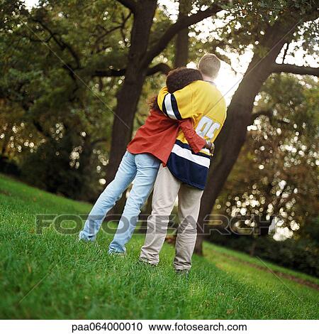 Young man and woman standing on grass, embracing, rear view, full length View Large Photo Image Stock Image - Young man and woman standing on grass, embracing, rear view, full length. Fotosearch