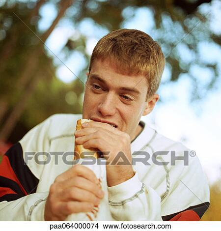 Young man eating sandwich outside View Large Photo Image Picture - Young man eating sandwich outside. Fotosearch