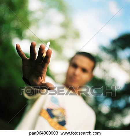 Stock Image - Young man holding out hand with cigarette, focus on foreground. Fotosearch