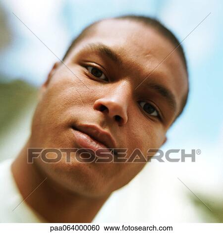 Stock Image - Young man looking at camera, low angle view, close-up, portrait.. Fotosearch