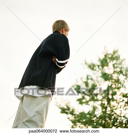 Stock Image - Young man standing with arms crossed, low angle view. Fotosearch