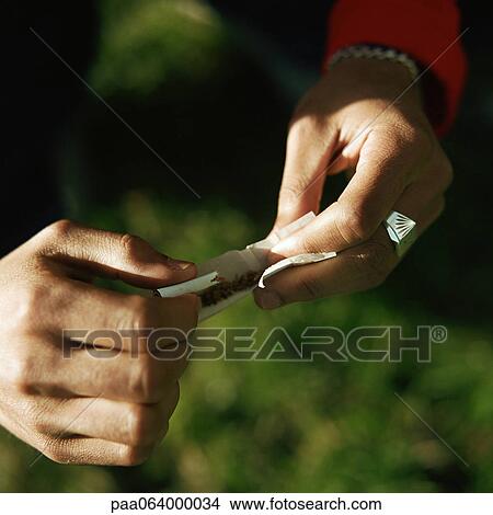 Picture - Young man's hands rolling cigarette outside, close up.. Fotosearch