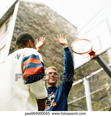 Stock Image - Young men playing basketball outside, low angle view. Fotosearch