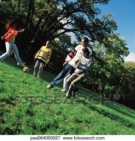 Stock Photo - Young people kicking soccer ball on grass. Fotosearch