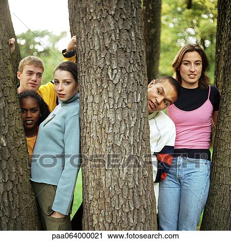 Stock Image - Young people standing between tree trunks, close-up.. Fotosearch
