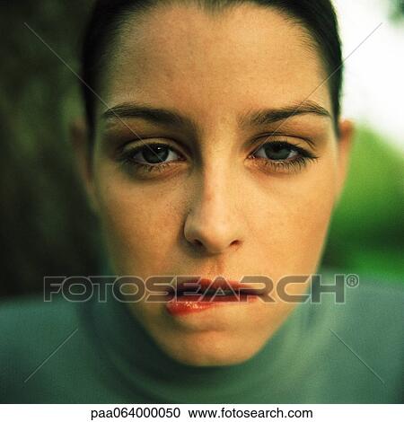 Stock Image - Young woman biting lower lip, looking at camera, close up, portrait.. Fotosearch