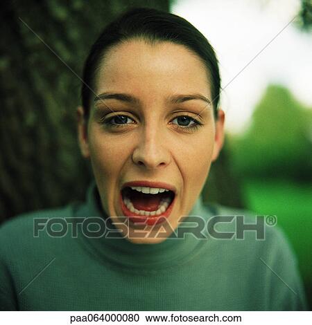 Stock Image - Young woman looking at camera with mouth open, close-up, portrait.. Fotosearch