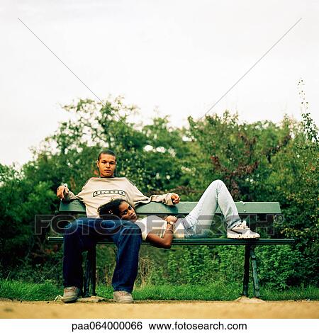 Stock Photograph - Young woman resting head on young man's lap, on bench outside.. Fotosearch