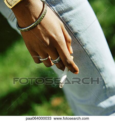Stock Image - Young woman's hand holding lit cigarette, close-up. Fotosearch