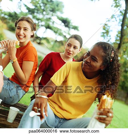 Stock Photograph - Young women eating sandwiches together outside. Fotosearch