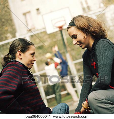 Young women sitting face to face, young men in background playing basketball. View Large Photo Image Stock Image - Young women sitting face to face, young men in background playing basketball.. Fotosearch
