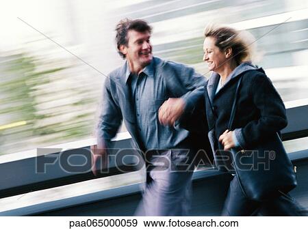 Stock Photo - Man and woman in coats walking, holding hands, blurred. Fotosearch