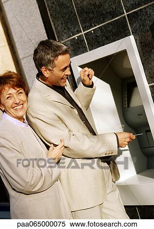 Man and woman in jackets at ATM machine, smiling View Large Photo Image Stock Photography - Man and woman in jackets at ATM machine, smiling. Fotosearch