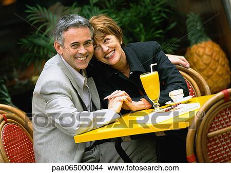 Picture - Man and woman sitting at table leaning close together, portrait.. Fotosearch