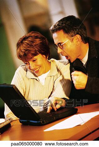 Man and woman sitting at table looking at laptop computer together. View Large Photo Image Stock Image - Man and woman sitting at table looking at laptop computer together.. Fotosearch