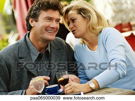 Stock Photo - Man and woman sitting at table, woman whispering to man, close-up. Fotosearch