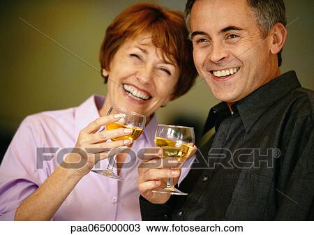 Stock Image - Man and woman smiling and holding up wine glasses, close up.. Fotosearch