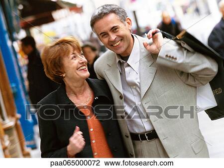 Stock Image - Man and woman walking together, man holding shopping bag over shoulder.. Fotosearch