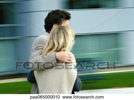 Stock Image - Man and woman walking together, man's arm around woman, blurred. Fotosearch