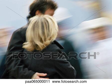 Stock Image - Man and woman walking together, man's arm around woman, blurred. Fotosearch