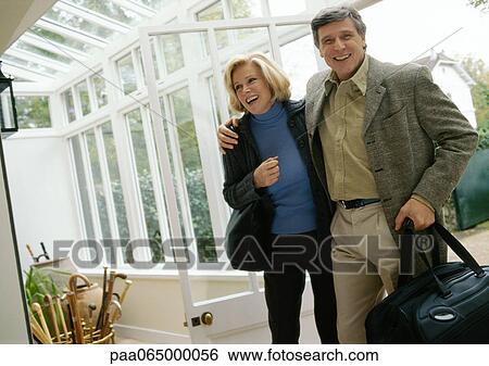 Stock Photograph - Mature man and woman standing together holding suitcase in doorway. Fotosearch