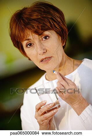 Picture - Woman holding pill and glass of water, close up, portrait.. Fotosearch
