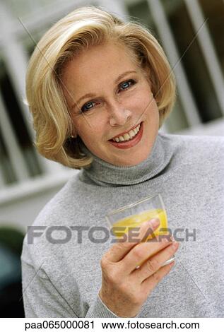 Stock Image - Woman looking at camera holding glass of orange juice, close up, portrait.. Fotosearch