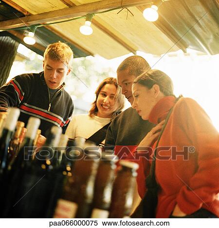 Stock Photography - Group of young people at outdoor market, bottled beverages blurred in foreground. Fotosearch